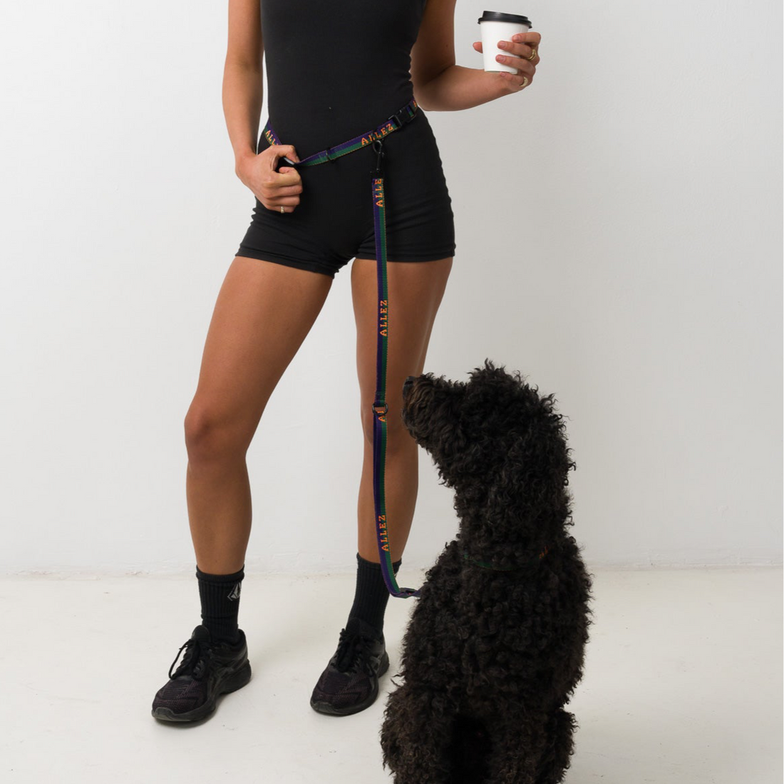 woman wearing and Allez hands free belt and lead system with a black cavoodle holding a coffee cup
