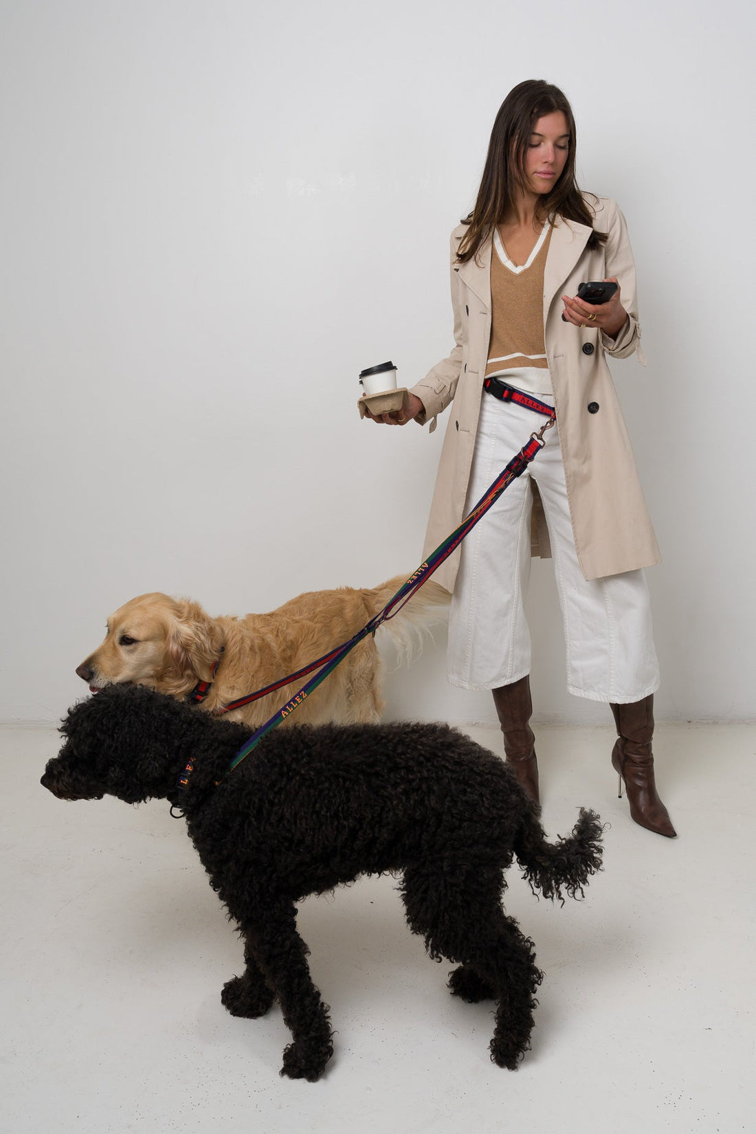 woman using a hands free Allez dog lead walking two dogs. One is large and one is a medium dog. This allows the woman to hold a coffee and her phone whilst walking 2 dogs using the Allez hands free dog walking system