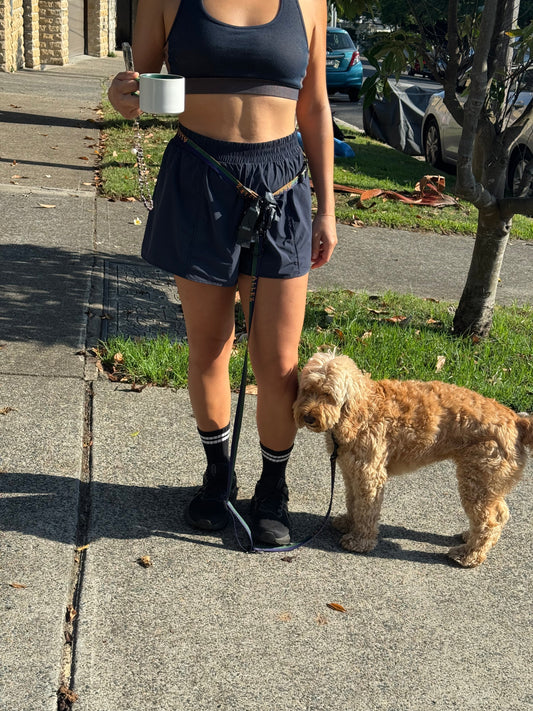 person holding a coffee cup and wearing a hands free Allez modular dog leash with a small cavoodle